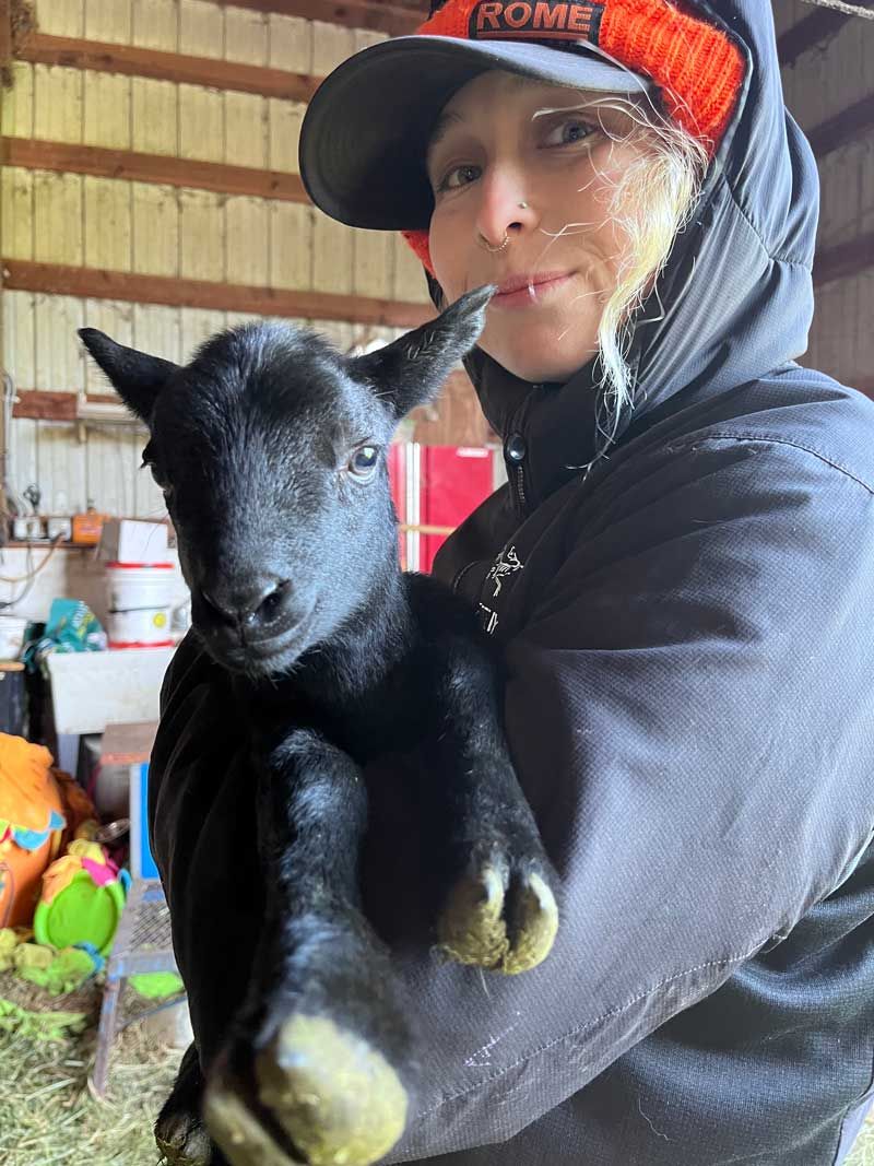 Bailey Stewart, Education Director at The Crest, holding baby Alpine Goat in the goat barn