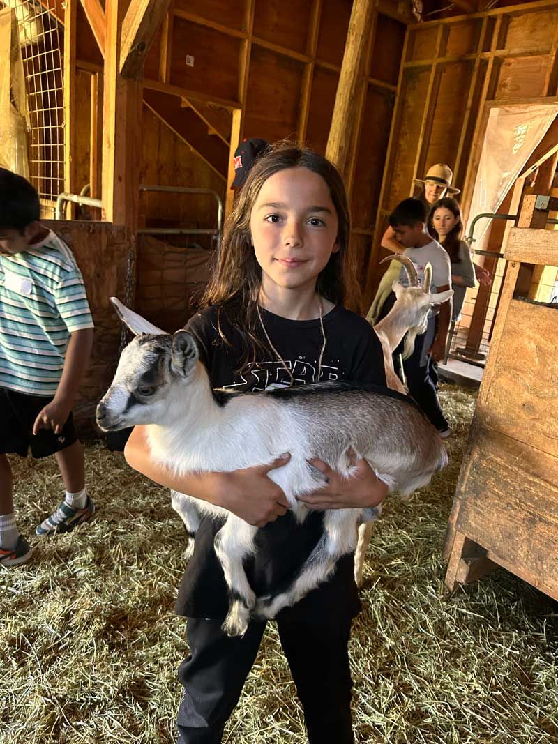 Nature Day Camp student shows how to hold a baby Alpine goat