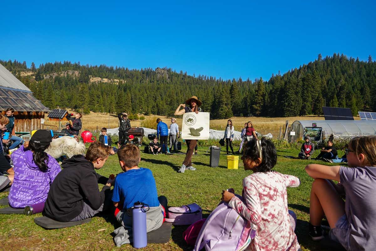 Education Director at The Crest talks to young students in circle during farm tour field trip