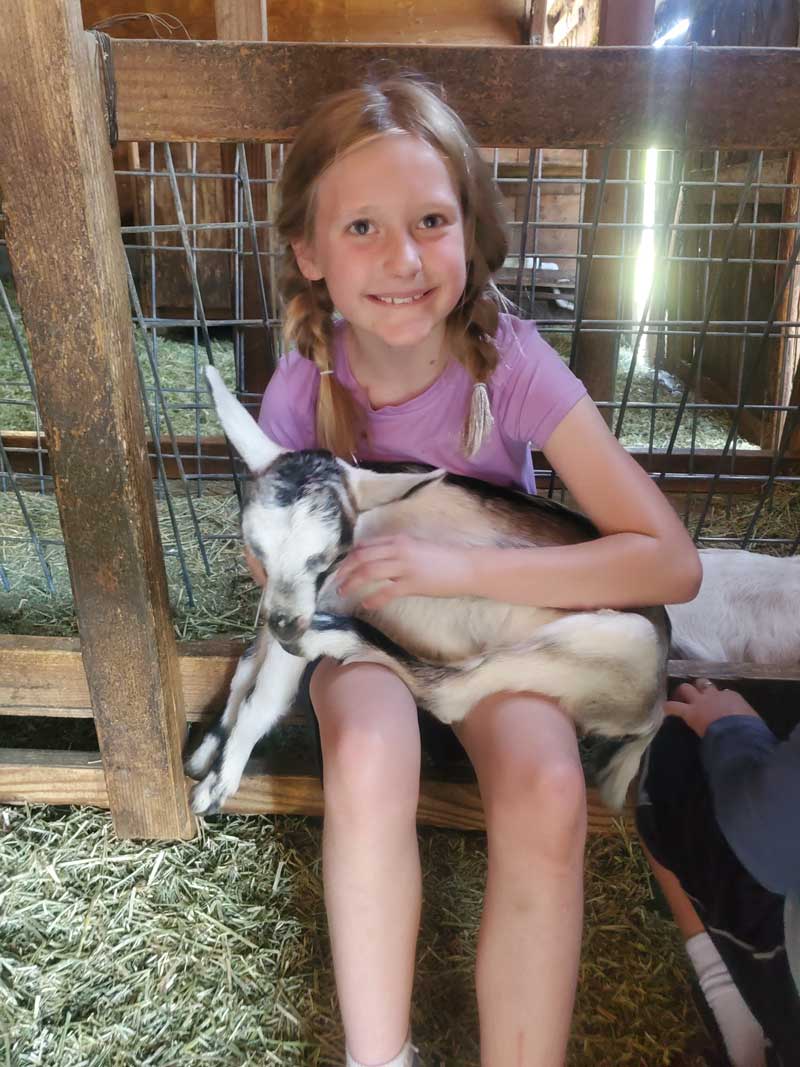 girl smiles while holding baby goat in her lap
