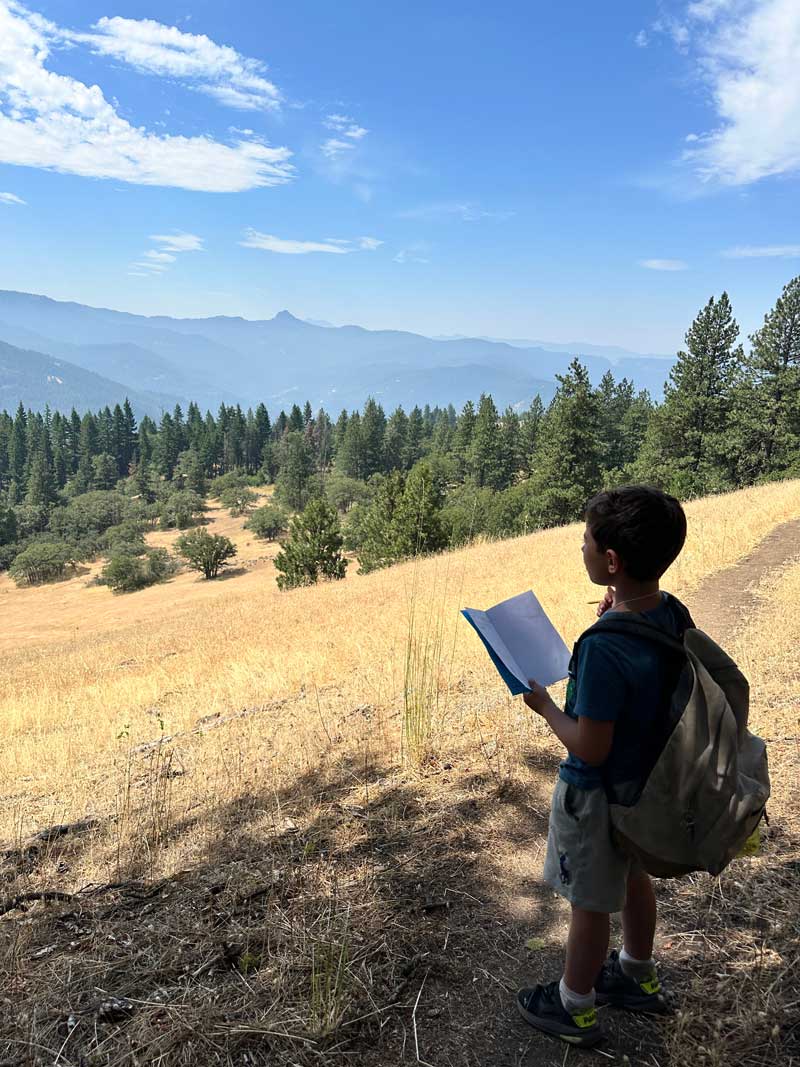 student with open journal admires mountain and valley views