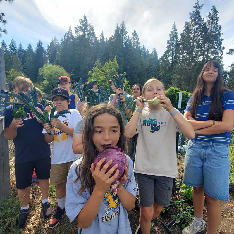 group of students pretend to eat the fresh picked garden produce in their hands