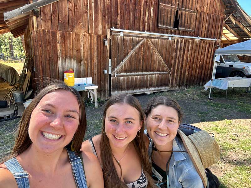 three smiling staff members in front of barn