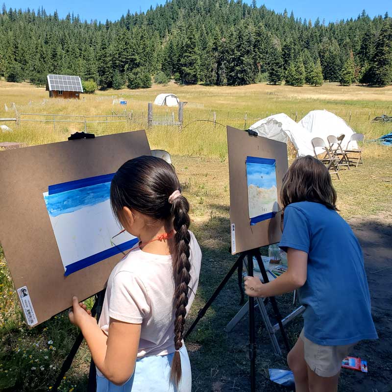 two students painting outdoors using easels